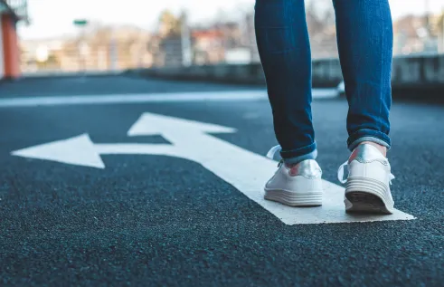 Person walking along a white arrow on road indicating two different directions