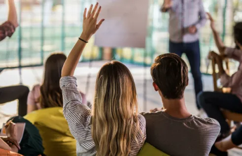 Students in a classroom raising their hands to ask a question