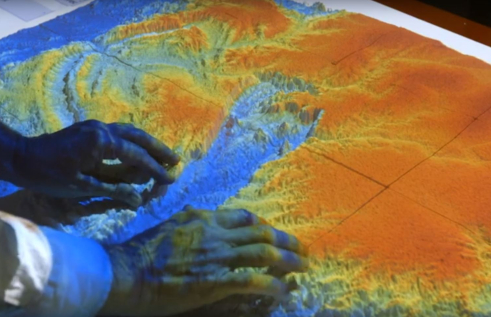 Hands atop a projection of a topographical landscape