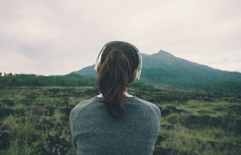 Female wearing headphones gazing into the distance overlooking a mountain