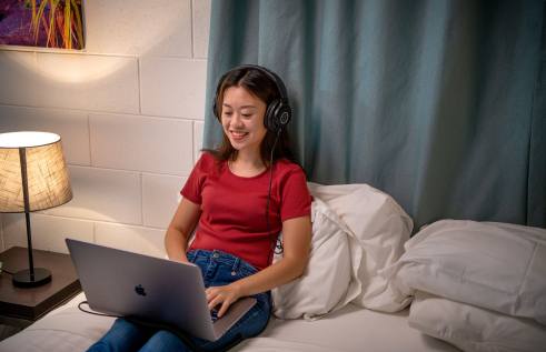 Female student smiling and looking at laptop while wearing headphones