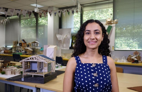 CDU student Nancy Soliman standing in the drafting studio in front of a model building.