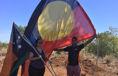 Luke standing outdoors raising a large Aboriginal flag