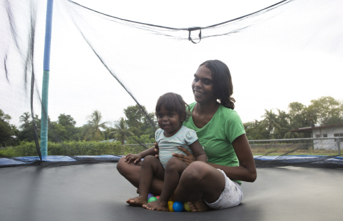 Indigenous Australian mother and her child sitting on a trampoline