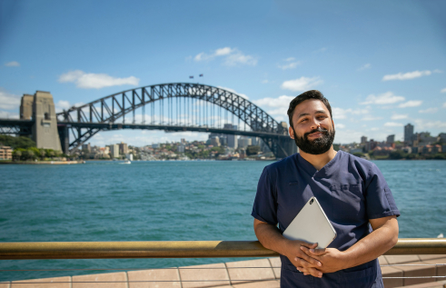 CDU nursing student in front of the Sydney Harbour Bridge holding a laptop