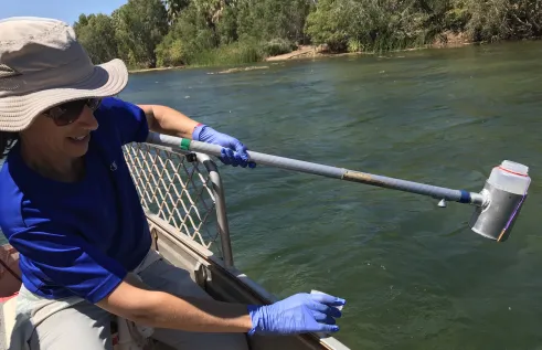 woman on a boat holding water sampling container on a long handle