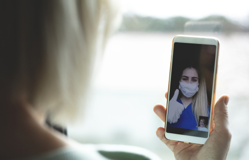 Stock image of a nurse in PPE talking to someone via telehealth or video conference