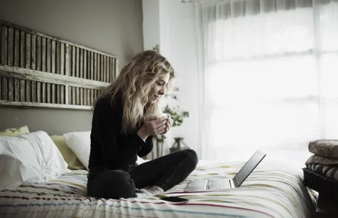 Stock image of female student studying online on her bed with a laptop