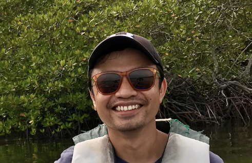 Sigit Sasmito, head and shoulders, wearing cap and sunglasses, with mangroves in background