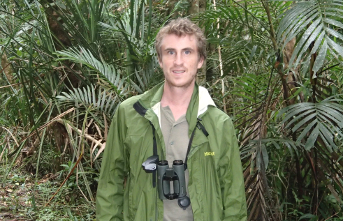 Simon Mahood with binoculars around his neck and palms in the background