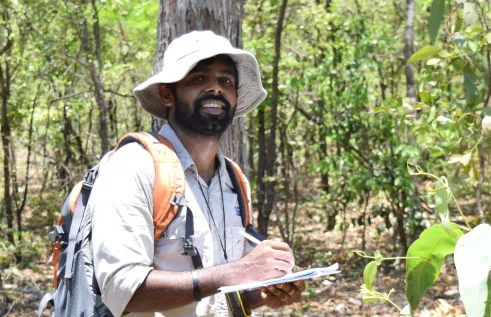 Man standing in forest writing in notebook