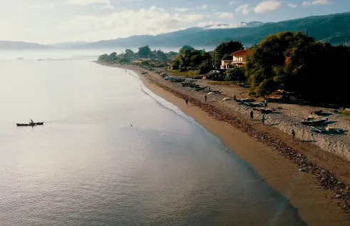 Aerial view of beach with people and boats, mountains in background