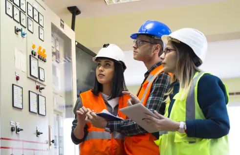 Three people in hi-vis vests looking at an electrical panel