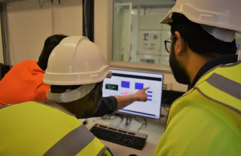 three people in high-vis, two with hard hats, looking at a computer screen