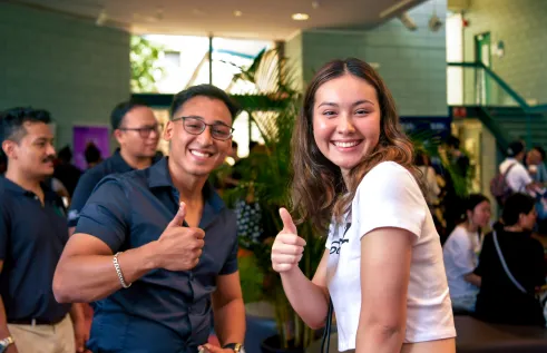 Two people posing with thumbs up. One person in dark button up shirt and another person in short sleeve white shirt.