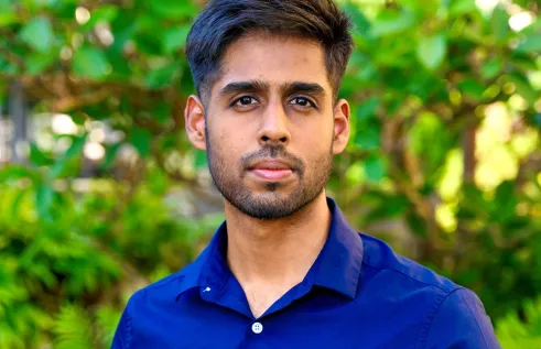 Young South Asian man looking straight at camera wearing vibrant blue collared shirt. 