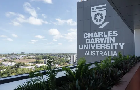 Image of University branding taken at elevation with the sprawling Darwin CBD in the background. 