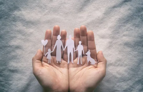 A person with open palms, holding a paper cut out of a family