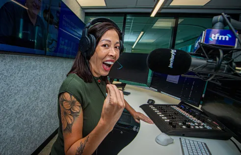 A woman stands in front of a mic in a radio studio. 