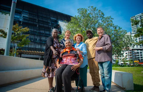 Six people stand in front of CDU's new Danala building - one lady is seated on a walker. Everyone looks happy. 
