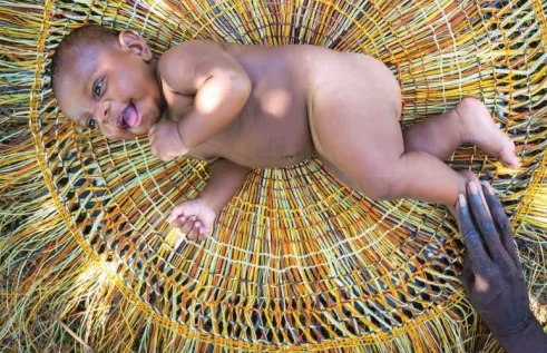 Mum touching baby smiling and lying on pandanus mat
