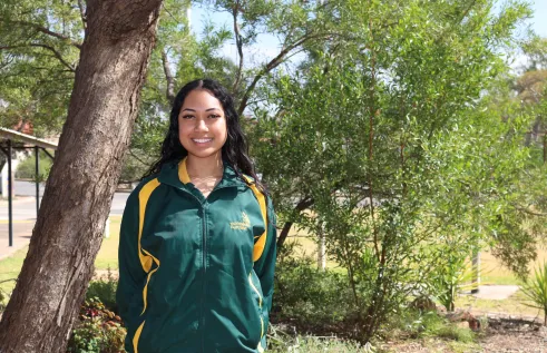 student stands outside in green and gold uniform