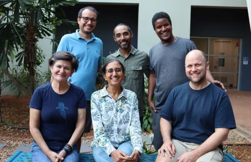six people, 3 seated,  standing behind them, posing for this photo, with a building and palm tree behind them