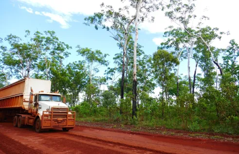 Truck driving on red mud road with forest in the back