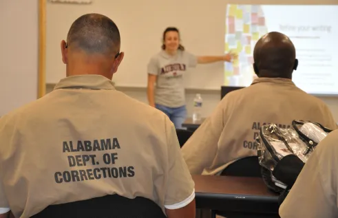 Men from corrections facility with back facing the camera, woman in the back standing and point at slides