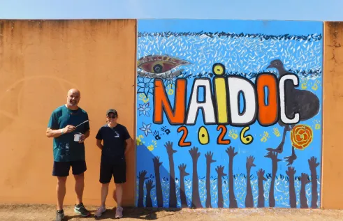 Charles Darwin University lecturers and Ywrite workshop facilitators Dean Mobbs and Adelle Sefton-Rowston next to a 2026 NAIDOC mural. Picture: Darwin Correctional Precinct