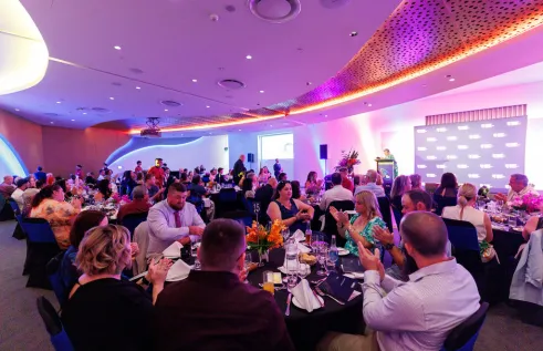 Fill room at gala dinner with people seated around tables and room lit up pink.