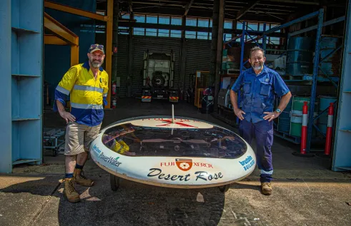 two males stand on either side of solar car