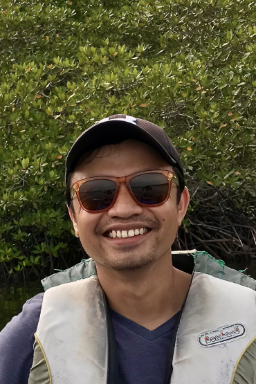 Dr Sigit Sasmito, head and shoulders, wearing cap and sunglasses, with mangroves in background