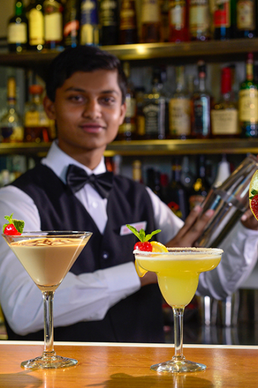 Student in training making colourful cocktails behind the bar