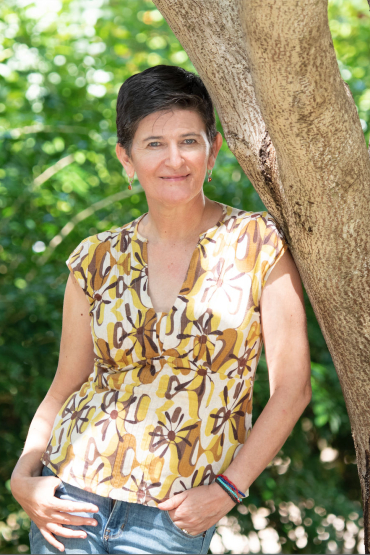 Veronica Toral Granda leaning against a tree trunk with green leaves behind