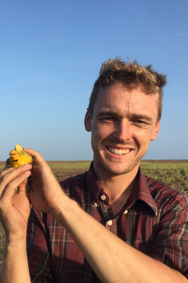 Robin Leppitt holding small yellow bird in open grassy landscape