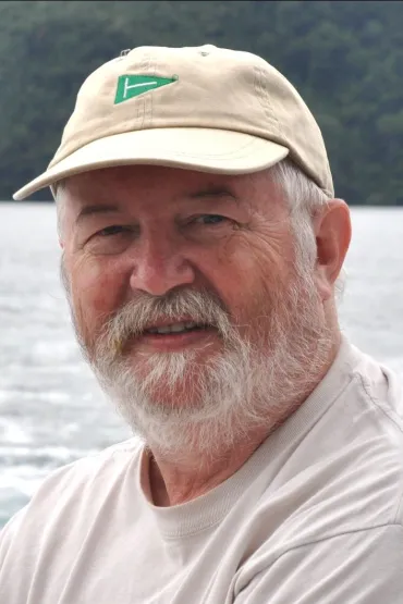Dr Julian Pepperell head and shoulders, wearing cap, with water and forest in background