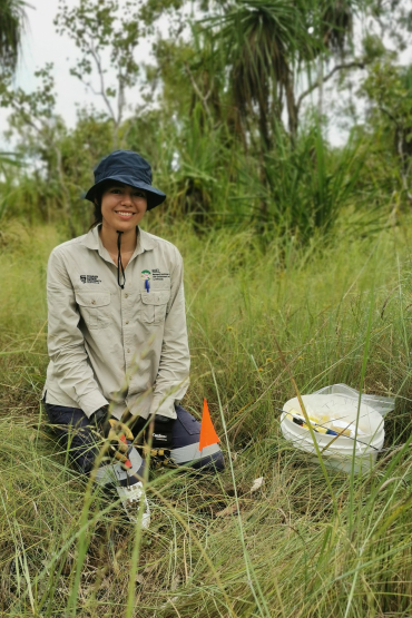 Alyson Malpartida kneeling in grass with a trowel in her hand and a white bucket