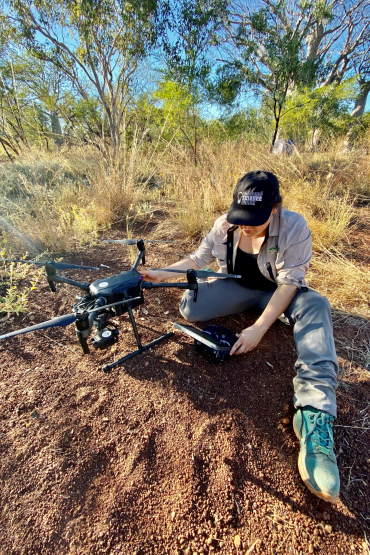 Dr Rebecca Rogers sitting on the ground next to a 5-rotor drone
