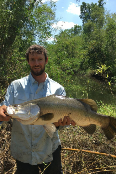 Brien Roberts holding a large fish, with bush and waterway in background