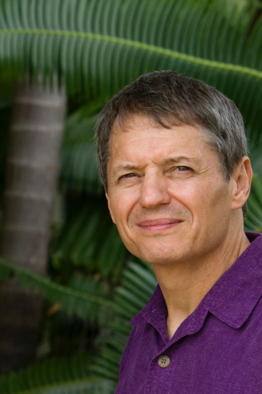 Keith Christian head and shoulders with palm tree trunk and large green leaves in the background