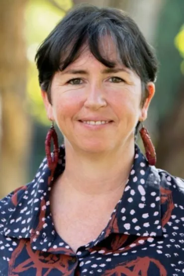 Billee McGinley head and shoulders, wearing blue with white dots and red patterns, with blurred background