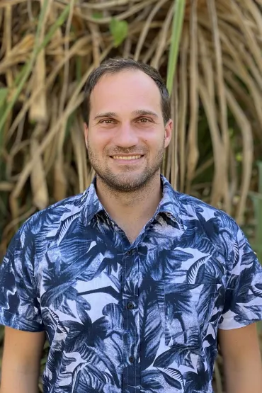 Dr Rafael Bohn Reckziegel, head and chest, wearing blue patterned shirt with long brown and green leaves in the background