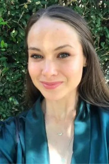 Young woman with brunette hair and blue shirt in front of hedge