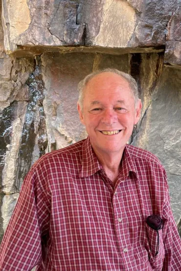 Steven Tickell, head and chest, wearing a red shirt with white cross hatching, with a rock face behind him