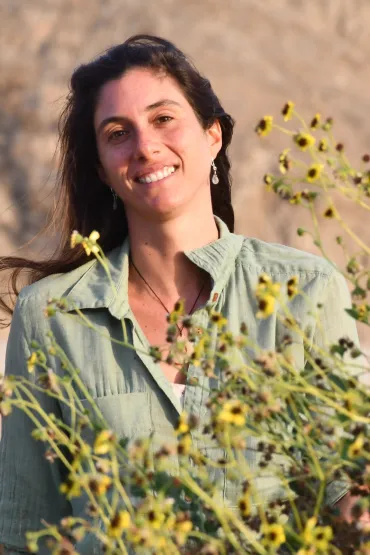 Adriana Gonzalez Pestana, head and upper body, with blurred background and yellow flowers in foreground