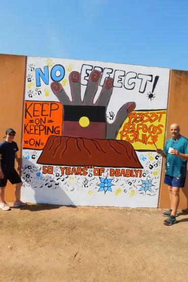 Charles Darwin University lecturers and Ywrite workshop facilitators Dean Mobbs and Adelle Sefton-Rowston next to a 2026 NAIDOC mural. Picture: Darwin Correctional Precinct